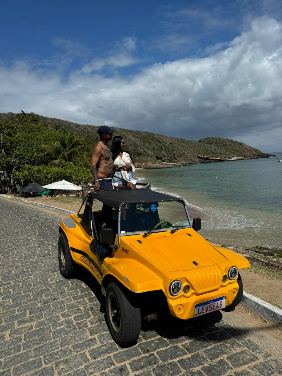 Couple on a yellow beach buggy on a coastal road in Búzios