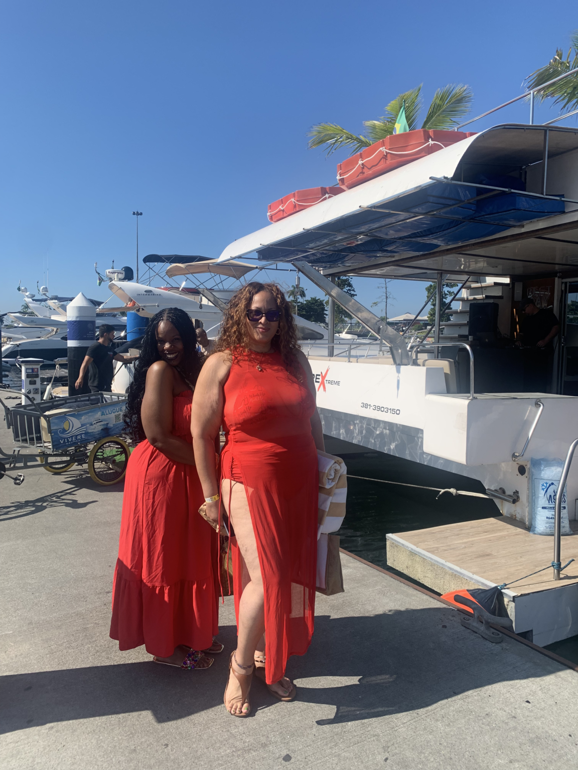 Two guests in red dresses beside a luxury catamaran at the marina in Rio de Janeiro