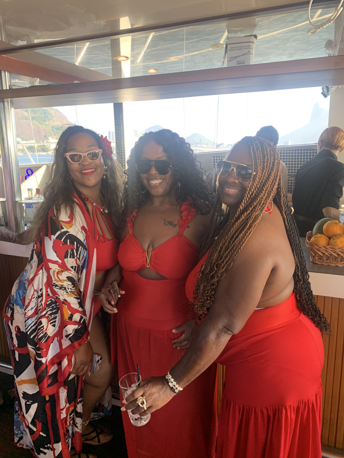 Three friends in red dresses smiling on board a luxury catamaran in Rio de Janeiro